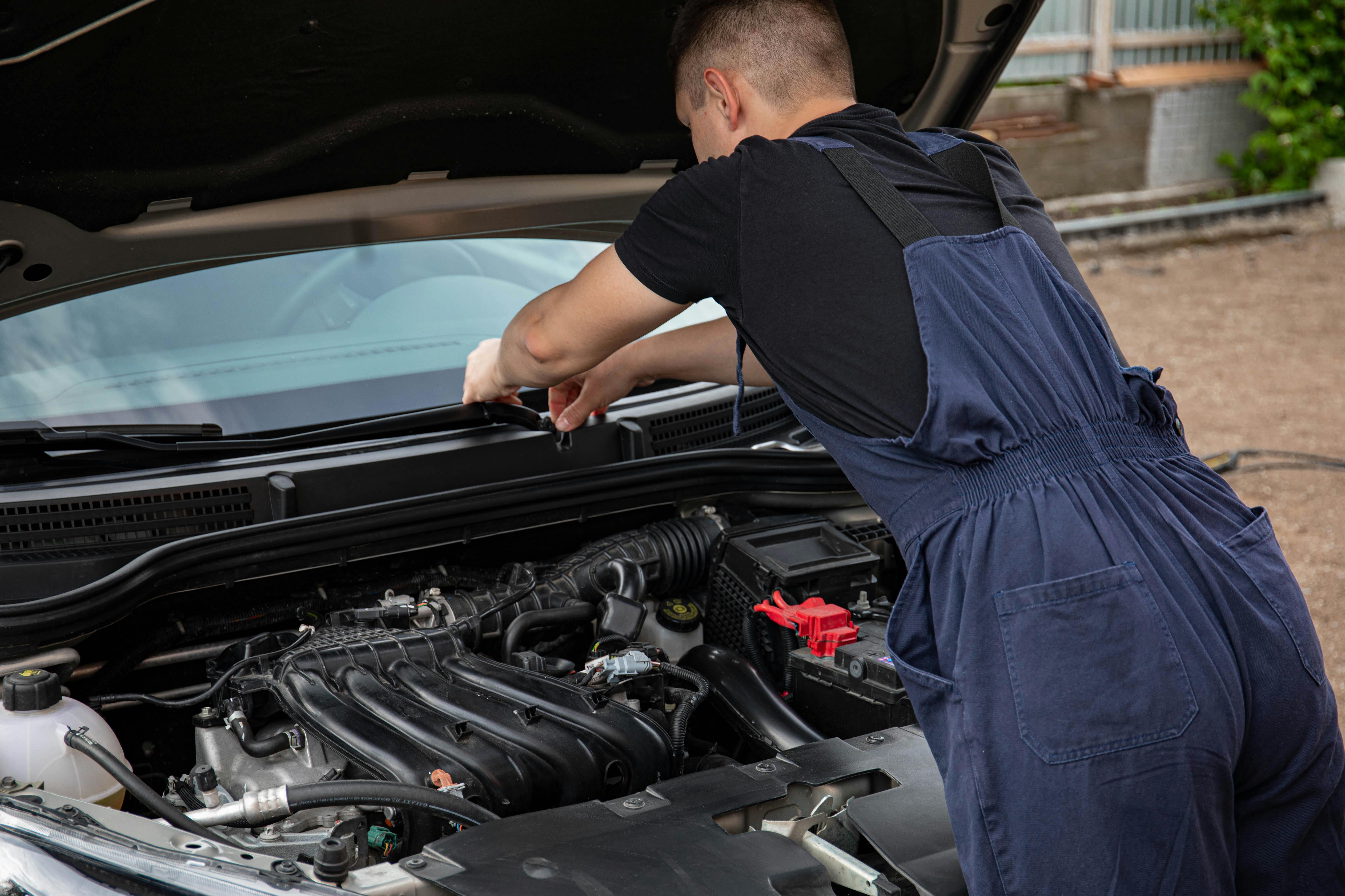 Outdoor engine-bay service with mechanic checking a vehicle before diagnostics.